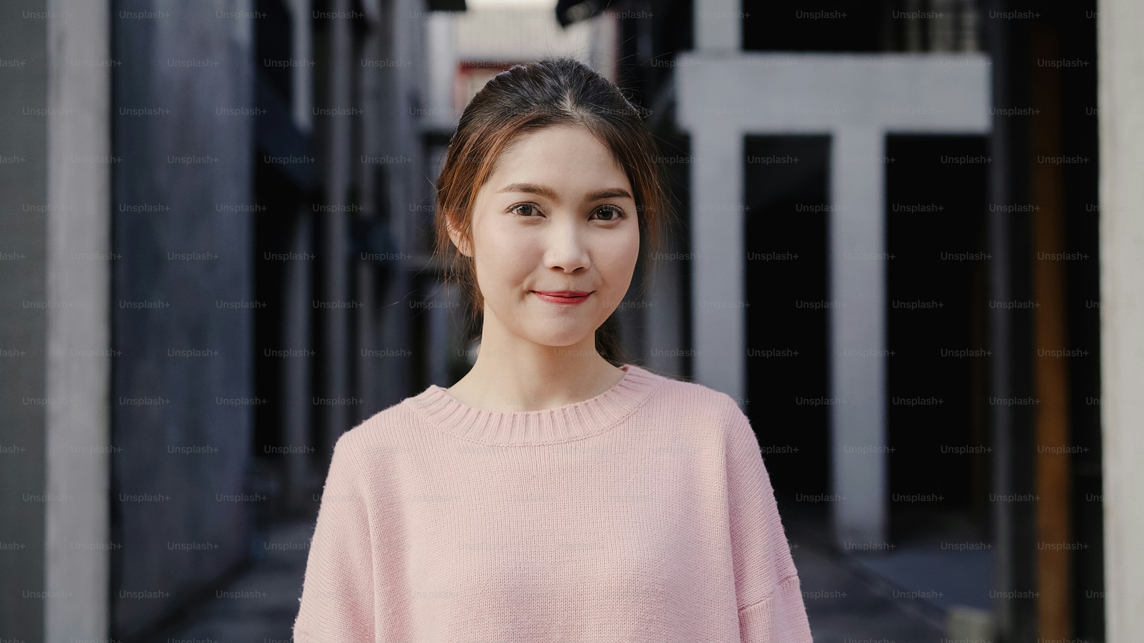 A woman in a pink sweater against a blurred architectural background
